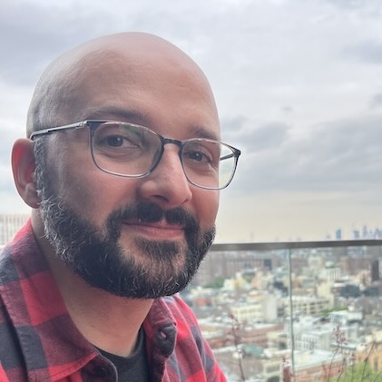 Josh Gister, a bearded man with glasses, on a rooftop with a city skyline behind him
